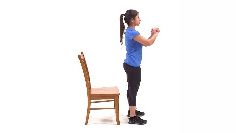 Person standing in front of a chair preparing to do a squat.