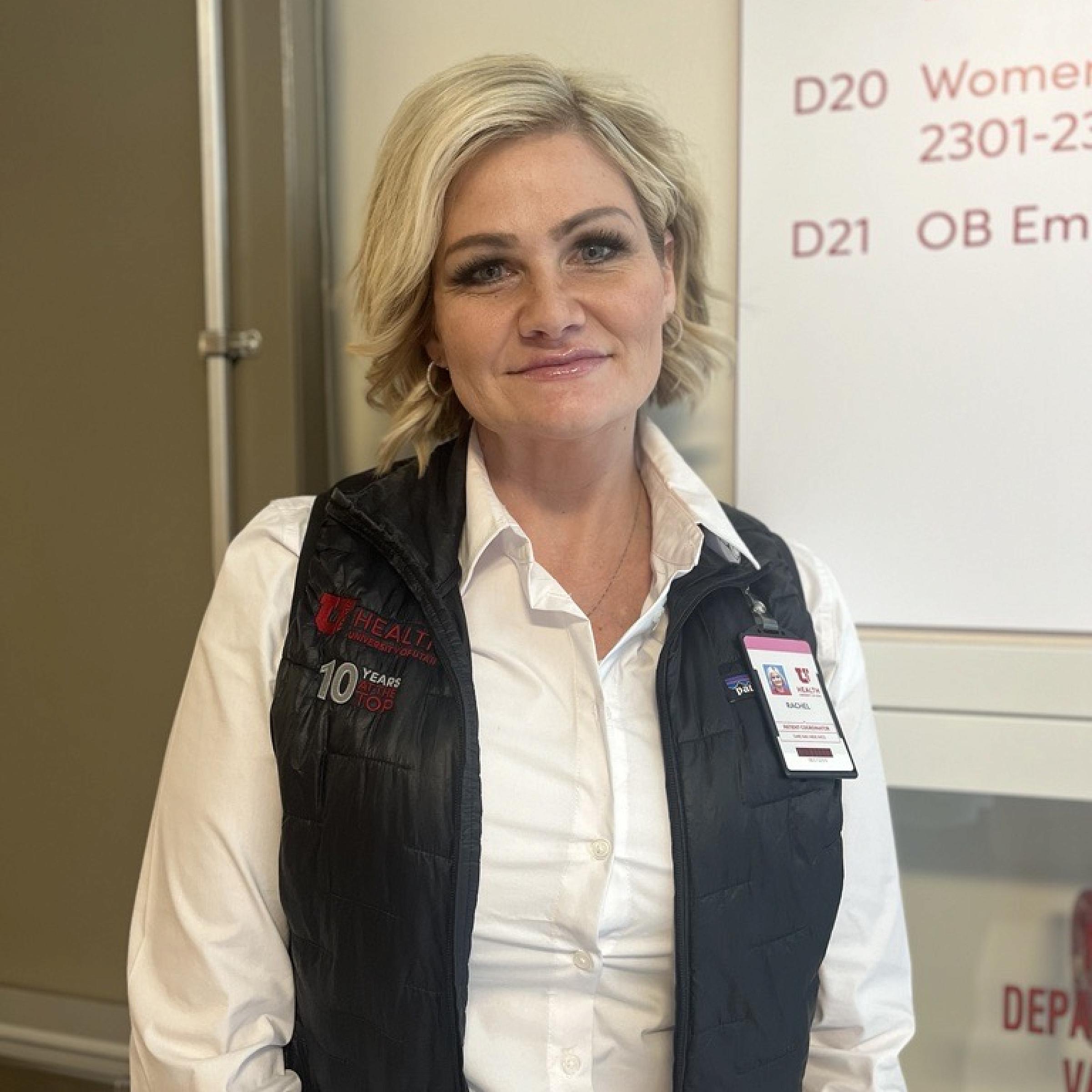 Rachel Harbert with short blonde hair wearing a U of U Health black vest stands in the hospital hallway.