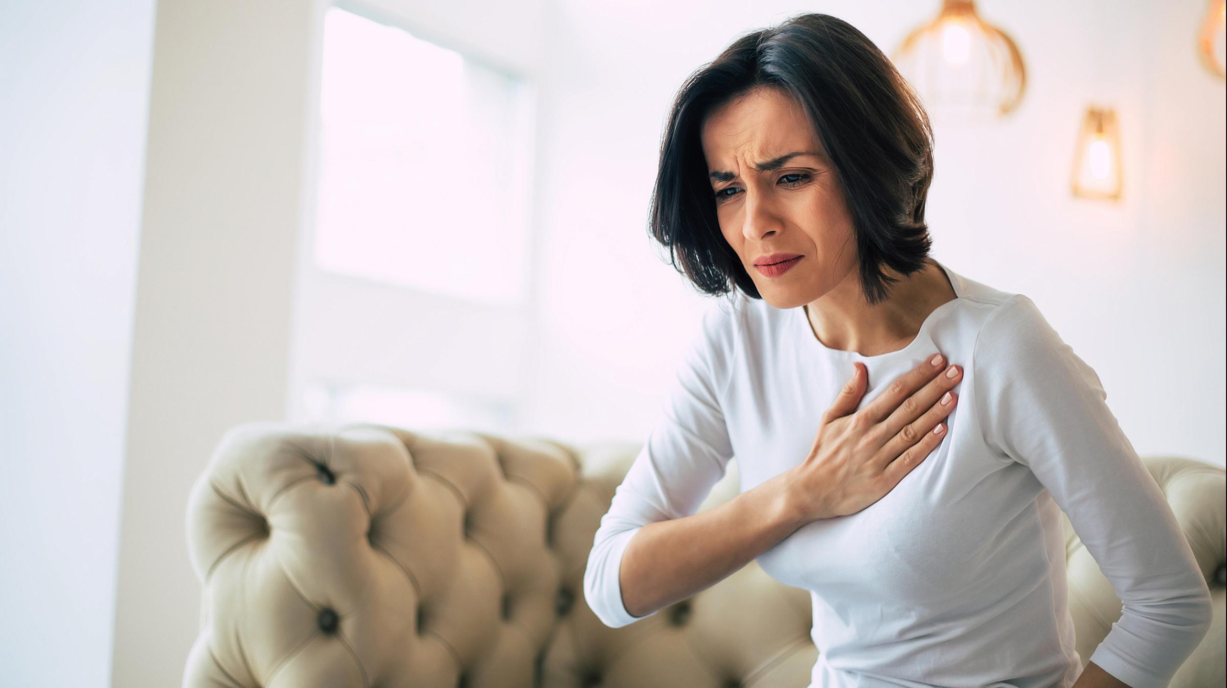 Woman sitting on couch with hand on her heart